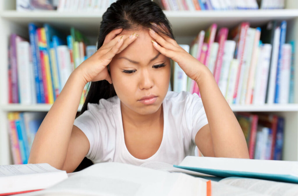 a young girl doing homework holds her forehead in frustration as she is having trouble reading