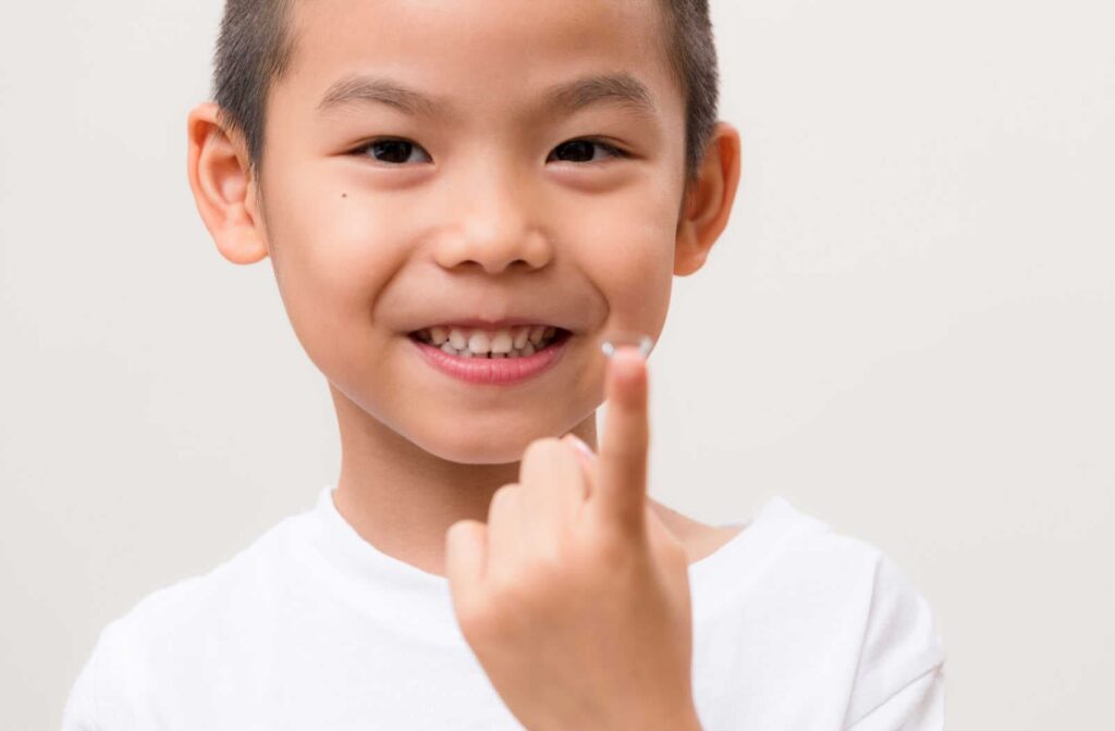 A young boy smiling while holding a contact lens on his finger as a method of myopia control