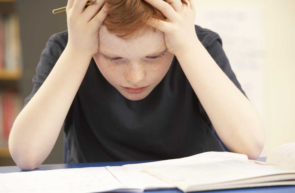 A student with his hands on his head because he is struggling to read in school, showing signs that he can benefit from vision therapy