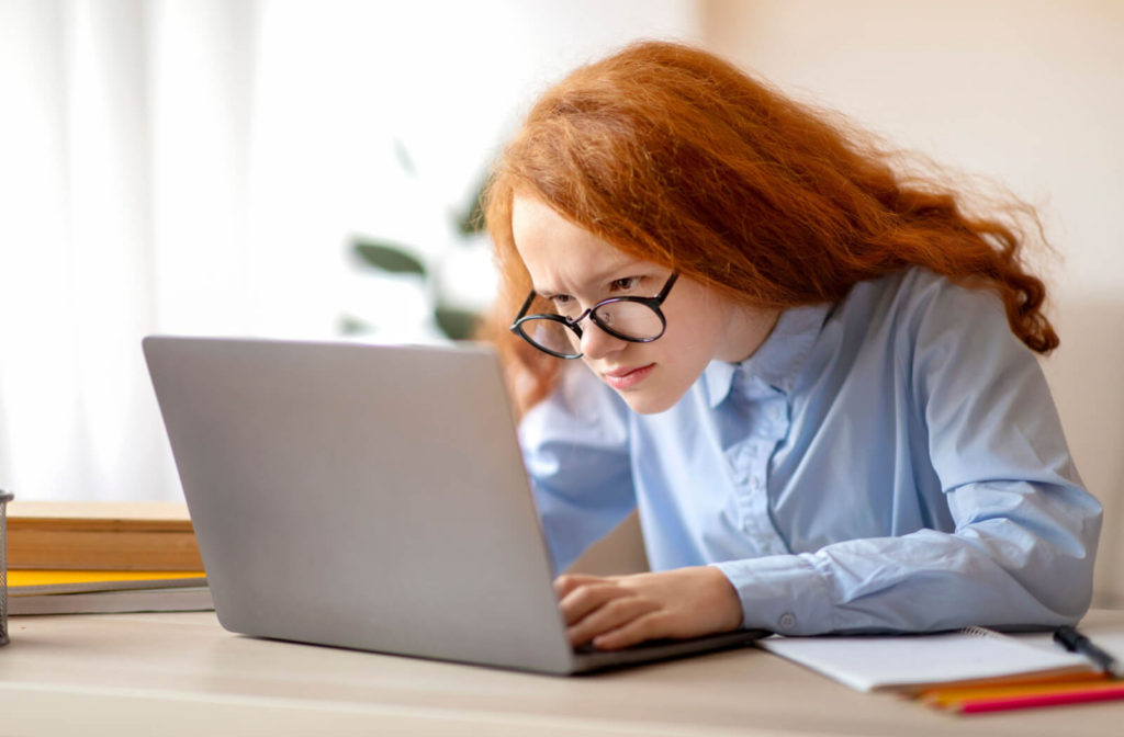 A red-haired girl leans closer to her laptop to see its content better.