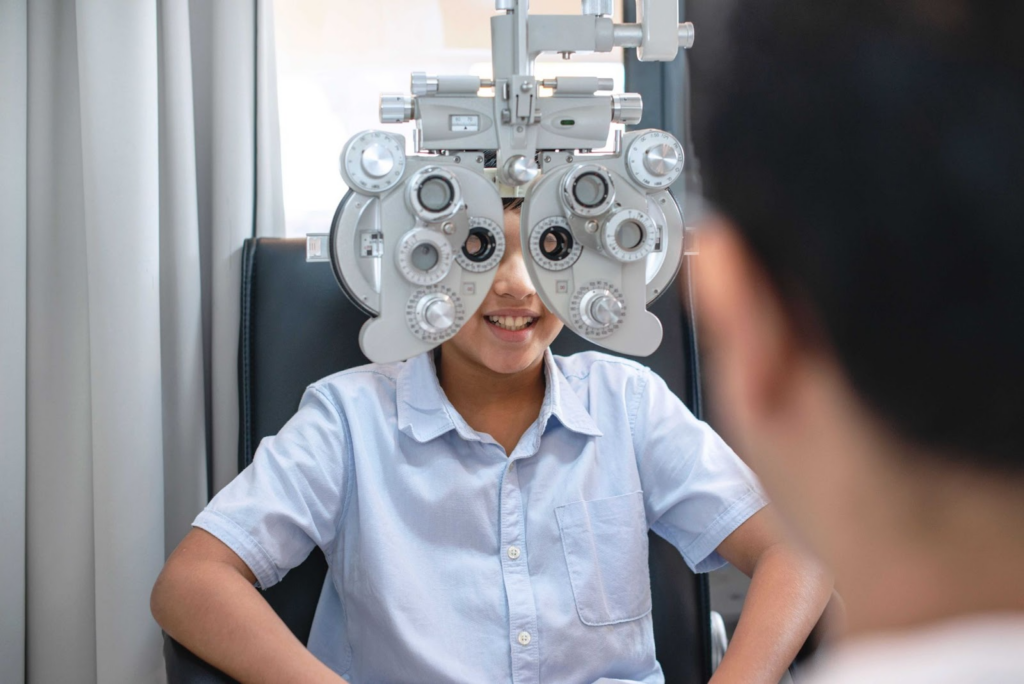 A young boy looking through a phoropter during a comprehensive eye exam