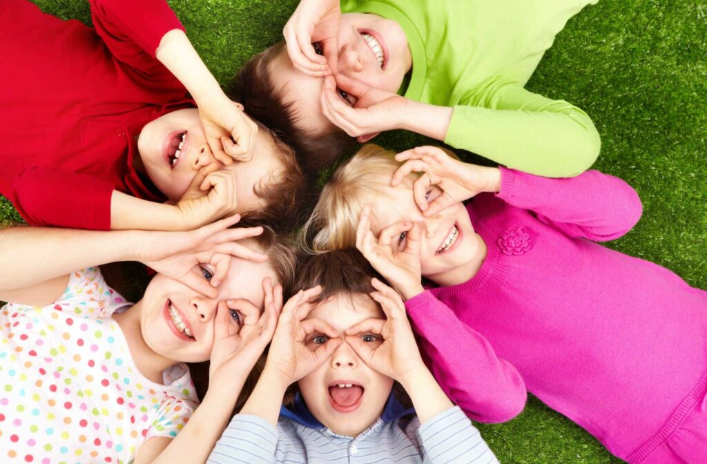 A group of kids laying in a circle outside making glasses to look through with their hands