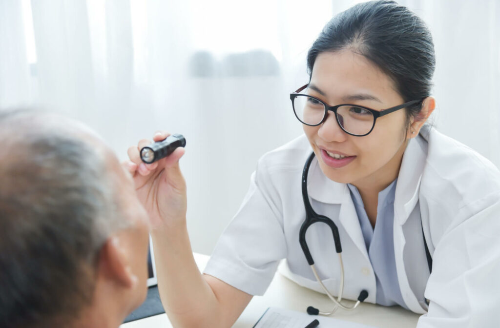 A senior man facing his optometrist as she shines a small flashlight into his eye