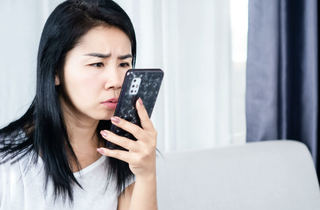 A woman sitting on a couch holding her smartphone very close to her face.