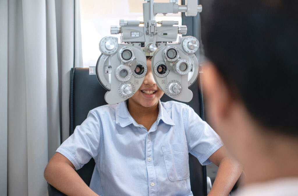A young boy looking through a phoropter during a comprehensive eye exam with an eye doctor.