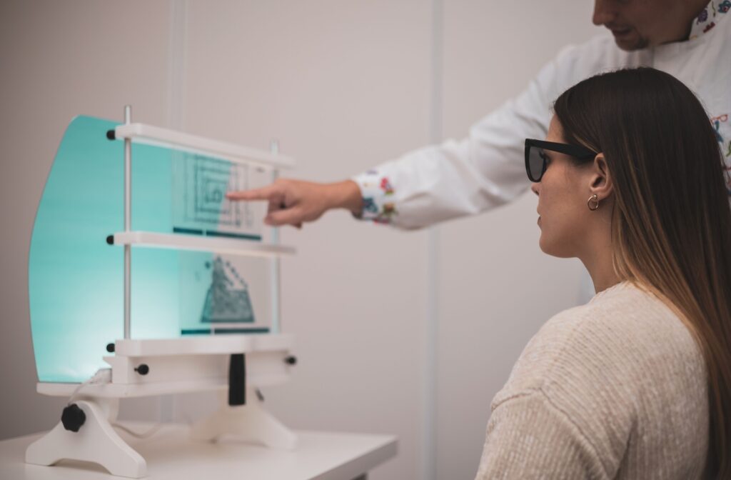 A young woman trying vision therapy in an optometry office while a male optometrist helps.