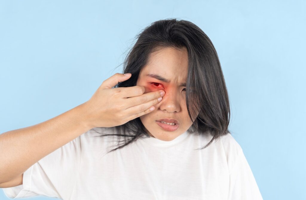 A young woman against a blue backdrop experiencing discomfort and pain in one eye from an inside out contact lens.
