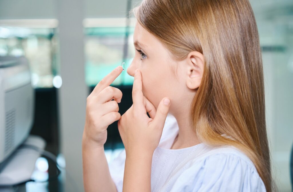 Side view of a young girl practicing putting on contact lenses. She holds her eyelid with a contact lens in the other hand.