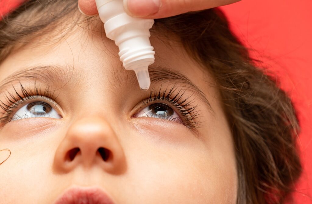 A child tilts their head back as their parent applies eye drops to them.