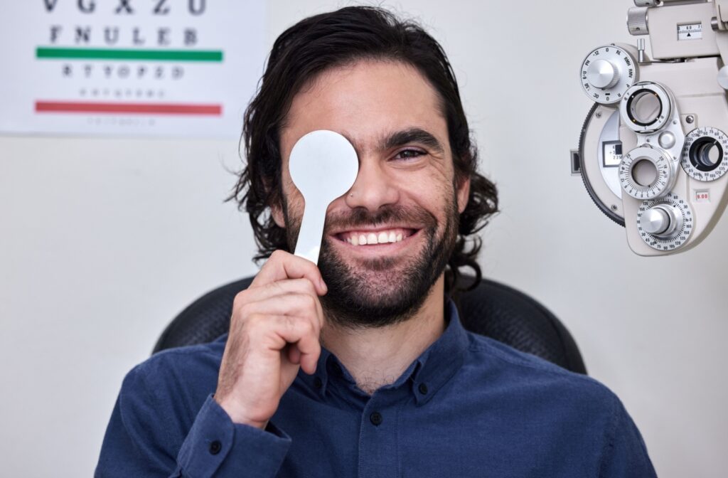 A person smiles while covering one eye with a vision test paddle during an eye exam.